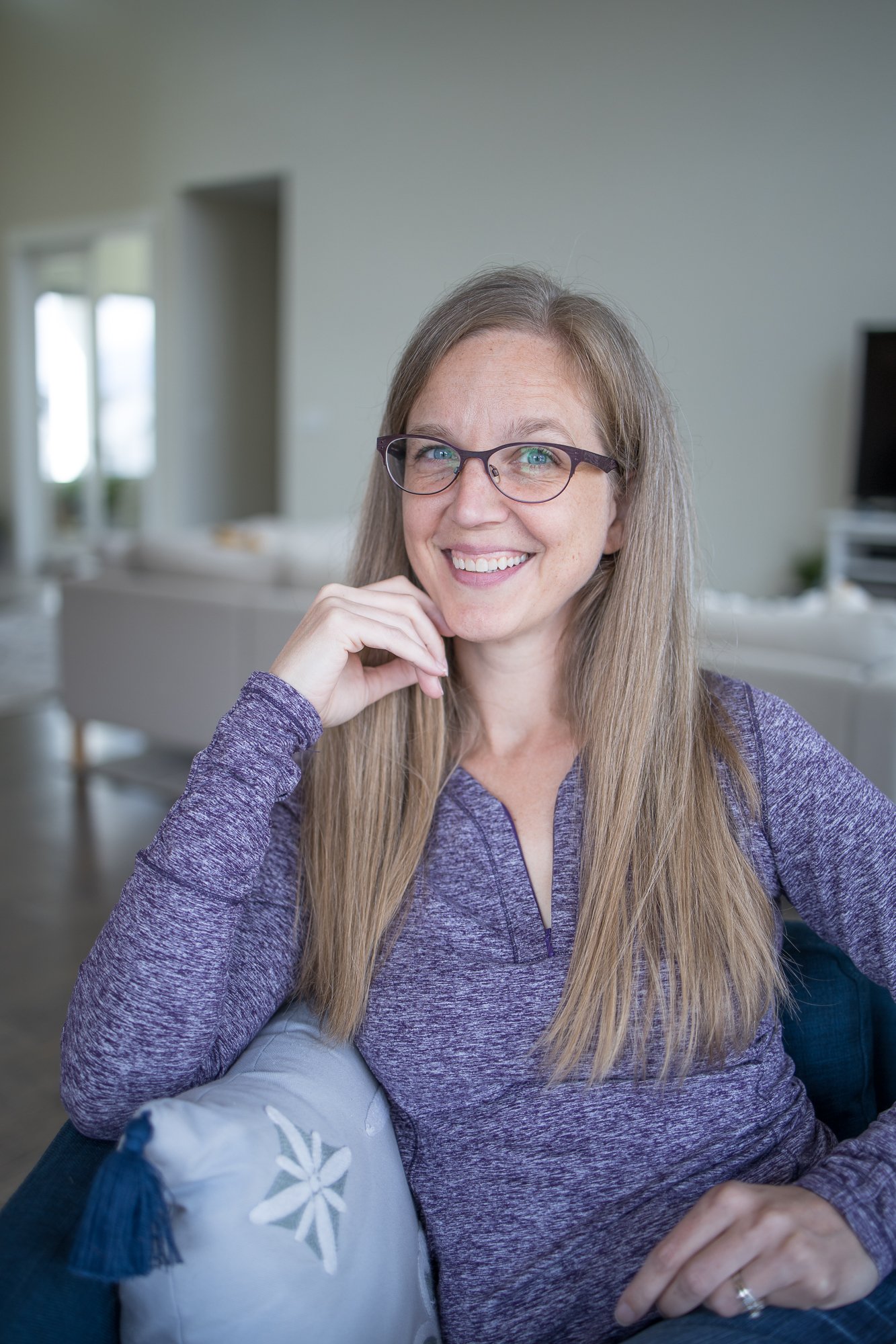 Esther Yunkin, RN. Host of the Health with Hashimoto's podcast. Professional headshot of a smiling Esther; long blonde hair and glasses, wearing a purple textured top and resting her chin on her hand in a softly lit indoor setting.